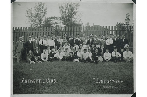 1914 photo of men and women posing in front of fence