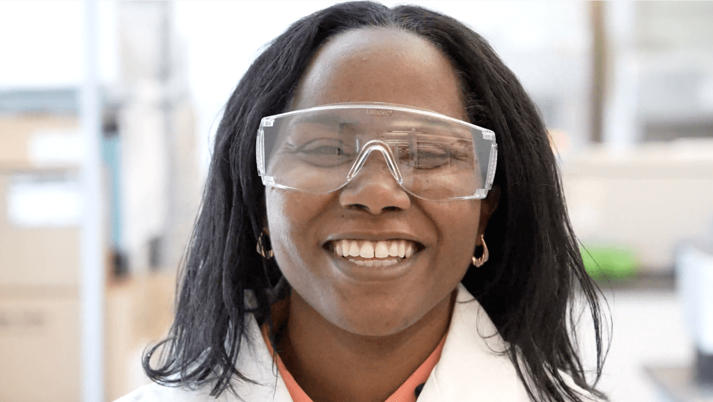 smiling woman wearing lab coat and goggles