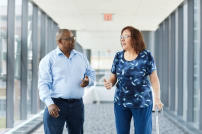 man and woman walking in the office. The woman has a cane.