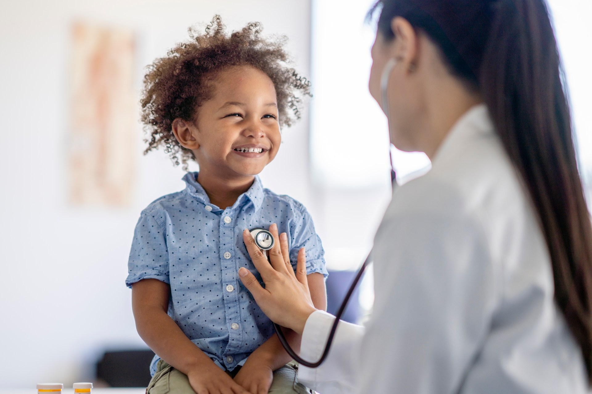 toddler smiling while female doctor listens to his heart with a stethoscope