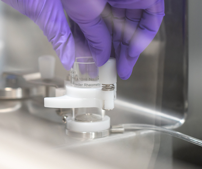 Gloved hand handling a small laboratory device labeled