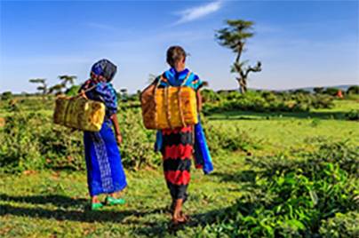 two women walking in nature carrying yellow bucket