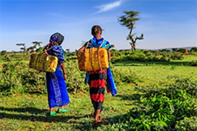 two women walking in nature carrying yellow bucket