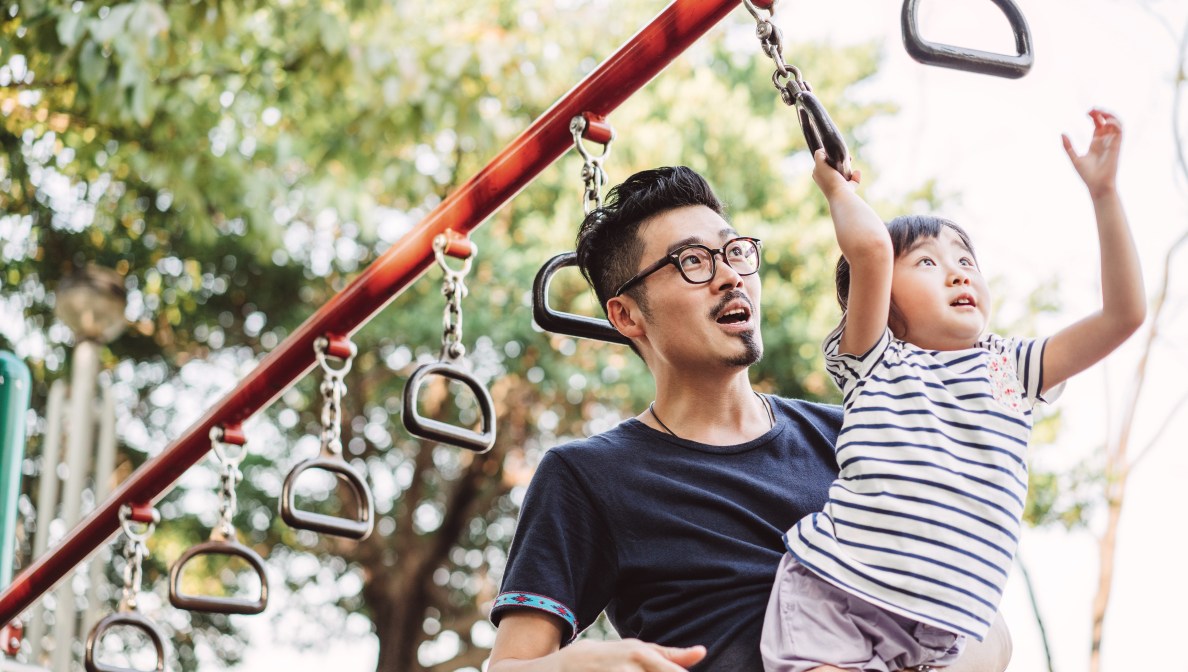 Adult holding a child while she hands on monkey bar
