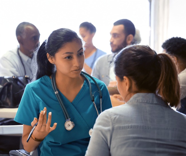 doctor with a patient in room full of another doctors and patients