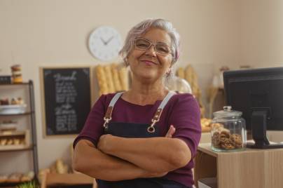 a person wearing an apron standing with arms across inside a bakery.