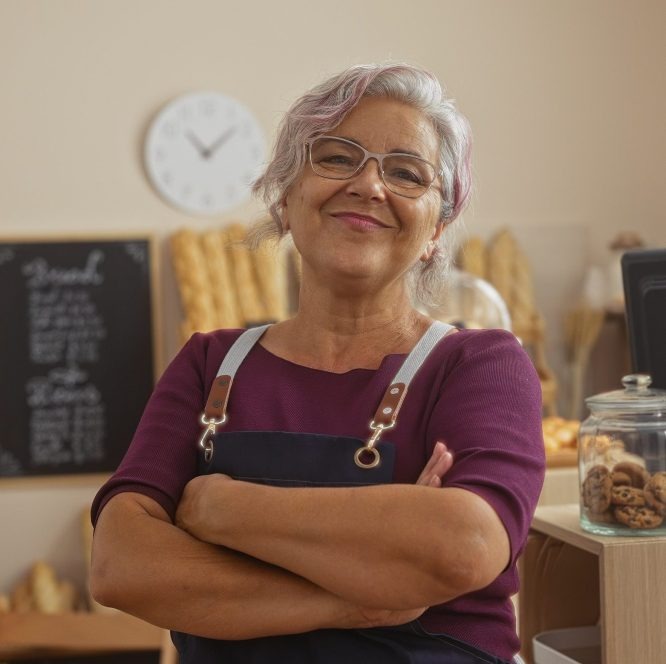 an older woman wearing an apron standing with arms crossed and smiling