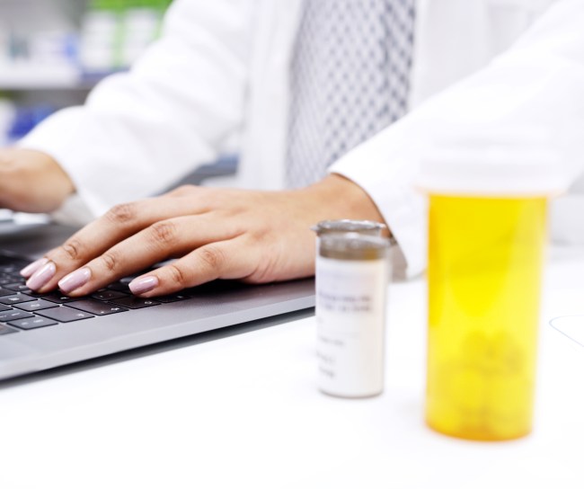 image of hands on a computer typing with pill bottles on the table next to the computer