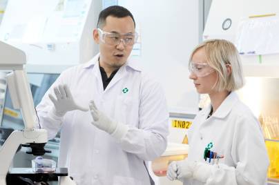 two scientists wearing lab coats and gloves working in a lab