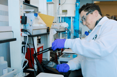 Merck scientist working in the lab. She's wearing a white lab coat and purple gloves.