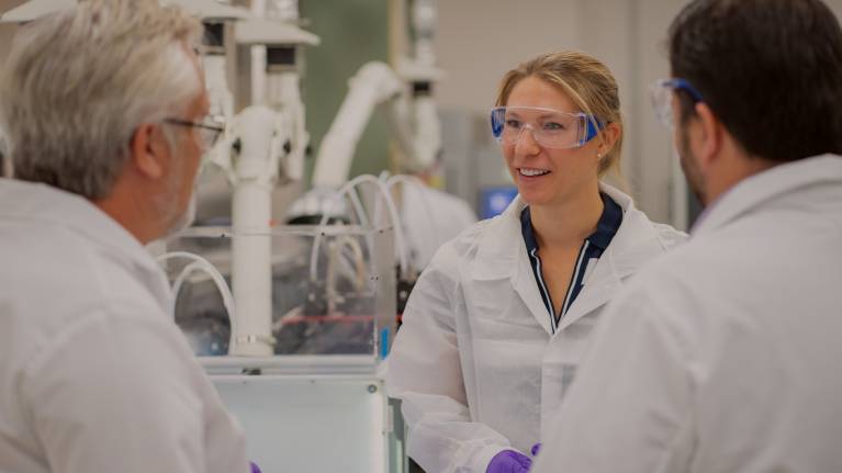 3 scientists wearing lab coats talking and smiling in a lab
